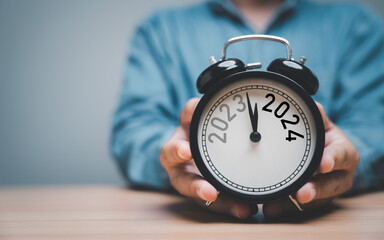 Wall Mural - businessman holding black alarm clock with change year from 2023 to 2024 with copy space , preparati