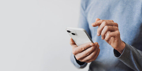 young man texting on smartphone over gray background. close up of adult male hand using mobile phone
