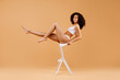 Young fit african american lady in underwear sitting on white chair and smiling at camera, posing on beige background