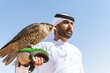 Middle-eastern emirati man wearing arab kandura holding falcon in the desert