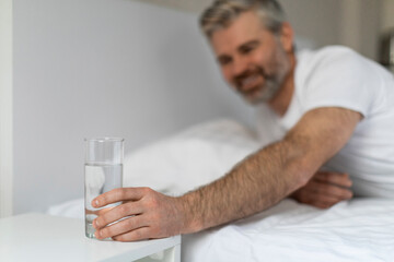 Wall Mural - Middle aged man reaching glass of water on bedside table