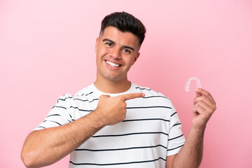 Wall Mural - Young caucasian man holding invisaling isolated on pink background and pointing it