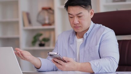 Upset asian business man in office using smart mobile phone failure. Cannot enter data no weak internet network. Male user frustrated by bad news signal service fail on smartphone app