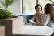 Cheerful businesswoman talk to colleague, company client, met in office sit at desk with laptop, discuss paperwork, contract details, sell services to customer take part in formal meeting, do business