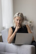 © fizkes - Thoughtful senior freelancer woman working at laptop from home, watching learning webinar, online content, using application, service for distant job, looking at screen, thinking