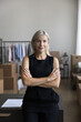 Positive confident middle aged small business owner vertical portrait. Happy successful mature entrepreneur woman, webstore manager, standing with arms crossed at storage place, looking at camera