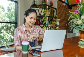 Asian businesswoman looking at watch smiling happily Satisfied with the confidence of working in an indoor office with a laptop computer. Job success concept.