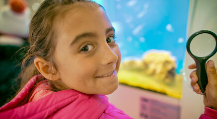 Poster - Young girl visiting city aquarium holding lens