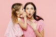 Happy woman wear casual clothes with child kid girl 6-7 years old. Mother daughter whisper gossip and tells secret behind her hand isolated on plain pastel pink background. Family parent day concept.