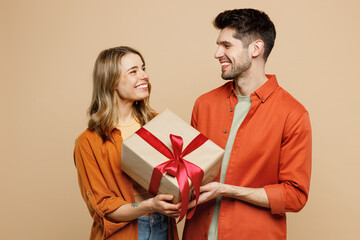 Wall Mural - Young fun couple two friends family man woman wear casual clothes looking camera hold present box with gift ribbon bow together isolated on pastel plain light beige color background studio portrait.