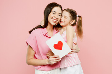 Wall Mural - Happy lovely woman wear casual clothes with child kid girl 6-7 years old. Daughter give mother postcard with heart, hug and cuddle isolated on plain pastel pink background. Family parent day concept.
