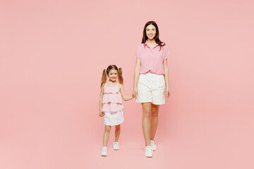 Wall Mural - Full body smiling woman wear casual clothes with child kid girl 6-7 years old. Mother daughter look camera hold hands walk together isolated on plain pastel pink background. Family parent day concept.