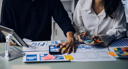 Close up ux developer and ui designer brainstorming about mobile app interface wireframe design on table with customer breif and color code at modern office.Creative digital development agency