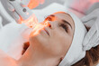 © YURIMA - Photo from the studio of cosmetology, demonstrating the process of led therapy and facial skin care. A woman undergoes a procedure in a beauty salon. Beautician in white gloves use