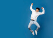 © Corina - Flull length image of a jumping teen boy in white hoodie and jeans, isolated blue background. Space for text.