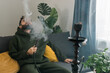 © satura_ - Bearded man is smoking hookah at home and blowing cloud of smoke - chill time and resting concept