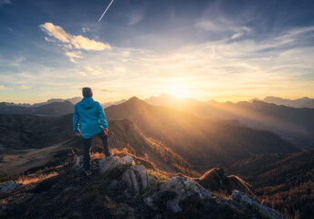 Wall Mural - Man on stone on the hill and beautiful mountain valley in haze at colorful sunset in autumn. Dolomites, Italy. Guy, mountain ridges in fog, orange grass and trees, blue sky with sun in fall. Hiking