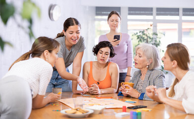 Mixed age group of positive friendly women studying together on cours, playing educational board game at table in classroom..