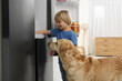 Little boy and cute Labrador Retriever seeking for food in refrigerator at home