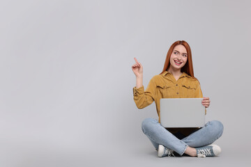 Wall Mural - Smiling young woman with laptop on grey background, space for text