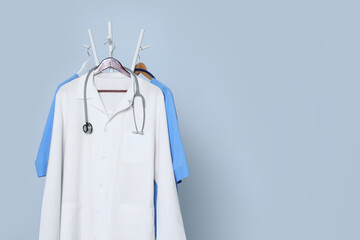 Poster - Medical uniforms and stethoscope hanging on rack against light grey background. Space for text