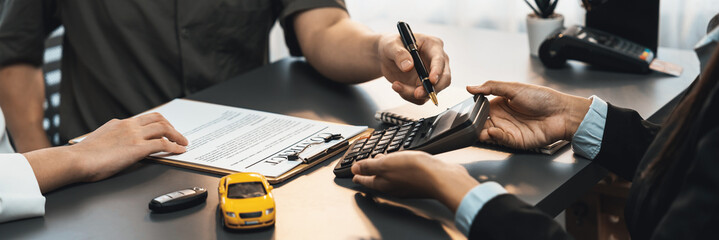 Car dealer calculate interest rate and costs of car loan with calculator, explaining details to customer on term and agreement in dealership office, offering financial and insurance service. Prodigy