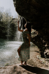 Wall Mural - Beautiful model in a turquoise dress posing near a mountain waterfall.Wildlife concept