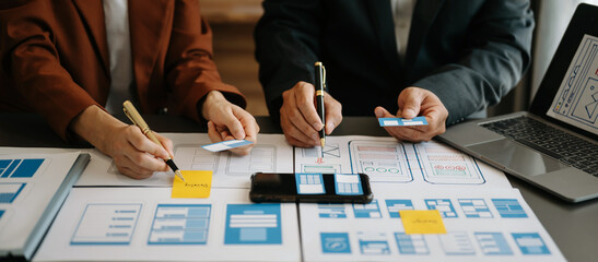  UX developer and ui designer brainstorming about mobile app interface wireframe design with customer breif and color code at office..