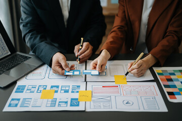  UX developer and ui designer brainstorming about mobile app interface wireframe design with customer breif and color code at office..
