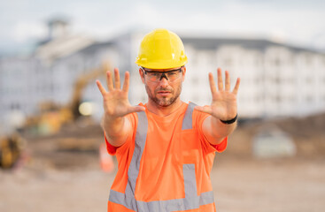 Worker with stop hand gesture. Builder in a hard hat working on a construction project at a site. A builder worker in a helmet near building construction sites. Builder on the job.