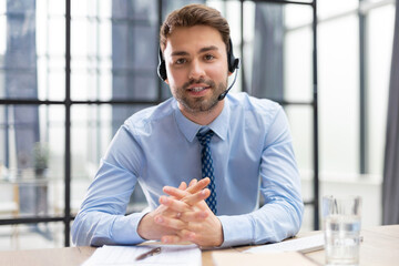 Sticker - Cheerful young support phone male operator in headset, at workplace with collegues on the background while using computer, help service and client consulting call center concept.