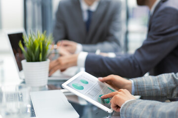 Business person analyzing financial statistics displayed on the tablet screen. Collegues on the background.