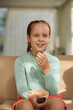 © DragonImages - Happy girl eating sweet snacks and watching tv at home