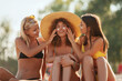 Three young women in bikinis, with sunscreen, happy smiling. 