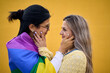Real couple of young women hugging and looking into each other eyes. Lesbians caressing face in loving attitude. Happy and nice people lgbt community on yellow background. Generation z.