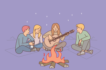 Friends are sitting around campfire with guitar enjoying camping and relaxation on evening beach