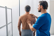 © Peakstock - Standing male patient has his spine investigated by osteopath. Osteopath examination