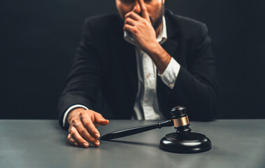 Focus gavel with blur lawyer sitting at his desk with worried and exhausted expression, feeling weight of pressure and stress of making hard decision on verdict with gavel hammer in hand. equility