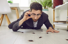 Funny Shocked Young Man Lying On White Wooden Floor In His House, Holding His Glasses, And Looking At Lots Of Disgusting Cockroaches Crawling Everywhere. Concept Of Roach Infestation At Home