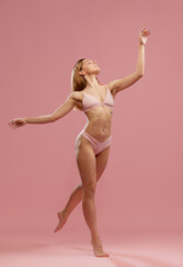 Portrait with dreaming young girl, model wearing beige seamless underwear posing on fingertips over pink studio background