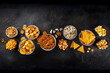 Salty snacks, party mix. An assortment of crispy appetizers, shot from above on a black background with copy space. Potato and tortilla chips, crackers, popcorn etc