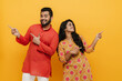 © Drobot Dean - Indian man and woman smiling pointing fingers at copy space in opposite directions isolated over yellow background