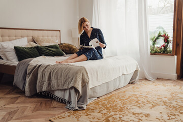 Wall Mural - Beautiful woman reading magazine while sitting in bed in her apartment