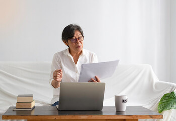 Old smart lady looking on paper and using laptop for working