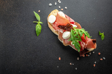 Wall Mural - Spanish Tapas with cured Slices of jamon iberico ham with basil on a dark background. banner, menu, recipe place for text, top view