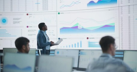 Fototapete - Male Project Manager Using Laptop And Analyzing Information, Graphs On Big Digital Screen In Monitoring Office. Black Man Working For Deep Learning Company, Diverse Employees Behind Desktop Computers.