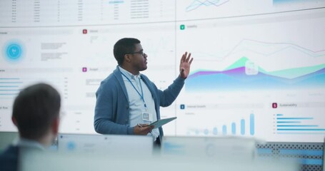 Fototapete - Black Male General Manager Giving Presentation To Consulting Company Employees On Big Digital Screen In Monitoring Room. Diverse Colleagues Listening to New Objectives Behind Desktop Computers.