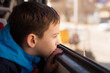 a cute boy in a bright sport jacket is riding alone on a tram and looks out the window. The boy's face is reflected in the window. Close-up