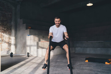 Wall Mural - Smiling young man doing ropes exercise in gym