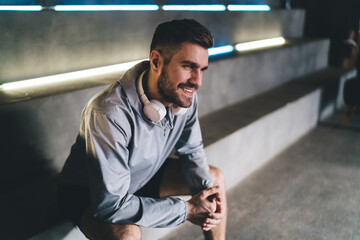 Wall Mural - Smiling sportsman sitting on stairs with lights in gym